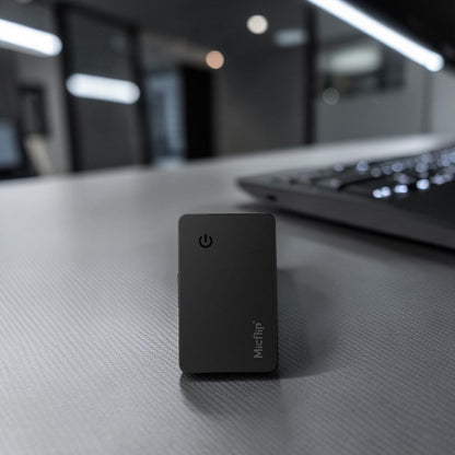 Micflip Ultra-Thin Wallet Card Finder in black, slim card-shaped device with Micflip branding, standing on a desk with a blurred laptop and office lights in the background.